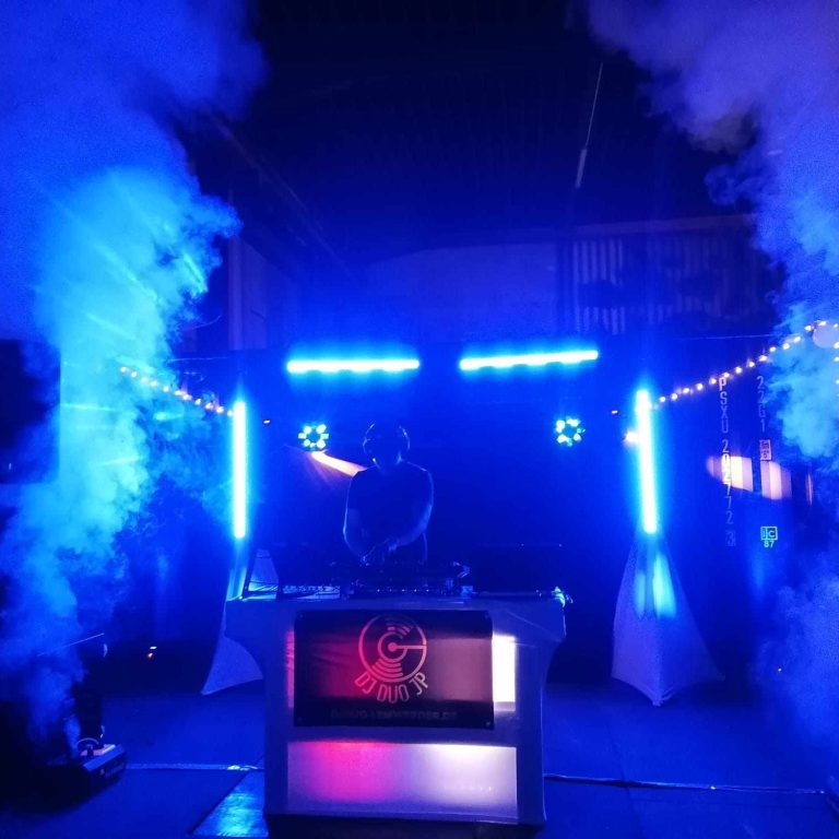 DJ an Pult umgeben von bunten Lichtern und Nebel, lebendige Partystimmung.
