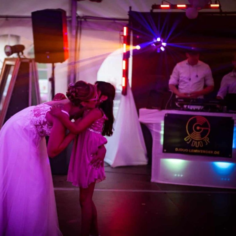 Braut umarmt ein Kind auf einer Feier mit DJ und bunten Lichtern im Hintergrund.