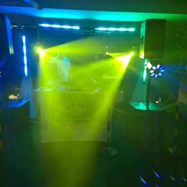 Beleuchtete Tanzfläche mit DJ und bunten Lichtstrahlen.