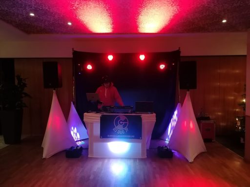 DJ-Pult mit Lichtern in Rot und Blau, umgeben von weißen Stoffen und Lautsprechern.