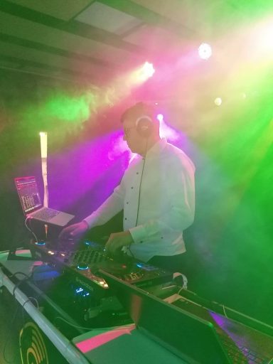 DJ in einem weißen Hemd arbeitet an einem Mischpult mit bunten Lichtern und Nebel.